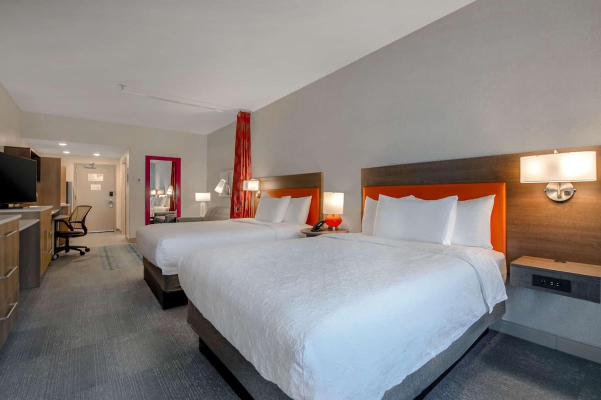 Habitació d'hotel amb dos llits, una taula de nit, una cadira, un televisor i un bany.