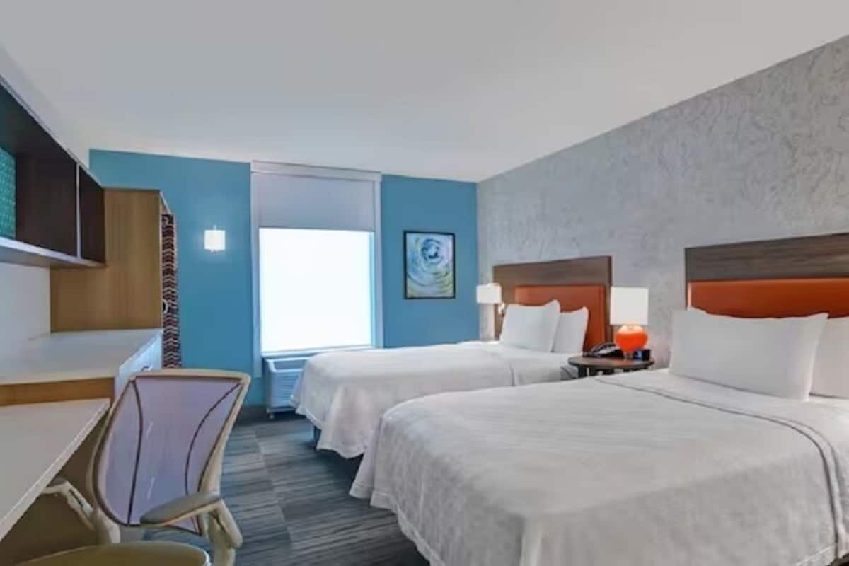 A hotel room with two beds, a desk, and a chair.