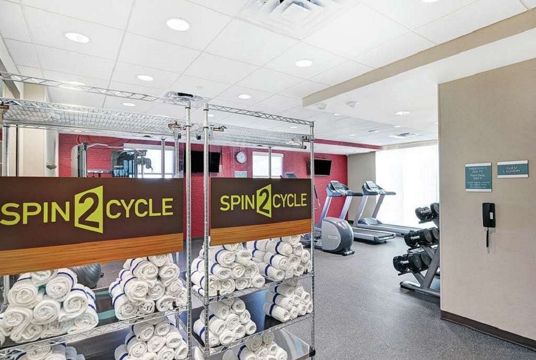 Une salle de sport arborant la marque « SPIN2CYCLE », équipée de matériel d’exercice et où des serviettes soigneusement pliées sont rangées sur des étagères.