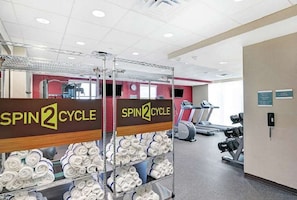Zona de gimnasio con la marca 'SPIN2CYCLE', equipo de ejercicio y toallas enrolladas ordenadamente en estantes.