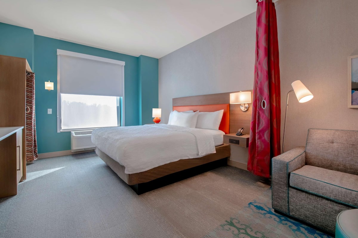 A hotel room with a bed, bedside tables, a chair, and a window with curtains.