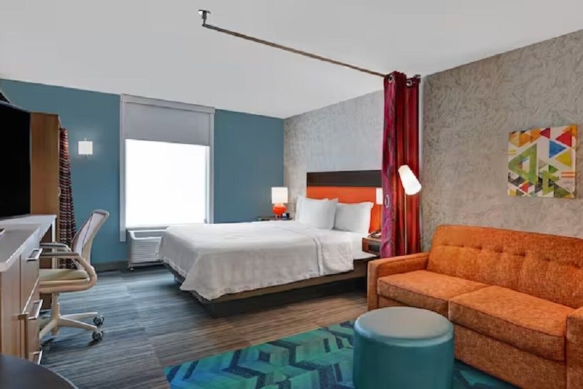 Una habitación de hotel con cama, sofá, escritorio, silla, lámpara y ventana.