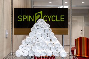 Une pile de serviettes enroulées, disposées en forme de pyramide, devant un panneau indiquant « SPIN2CYCLE ».