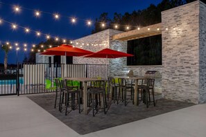 Une terrasse extérieure avec des tables et des chaises, des guirlandes lumineuses et une piscine en arrière-plan.