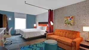 Une chambre d’hôtel avec un lit, un canapé, un bureau, une chaise, une lampe et une fenêtre.