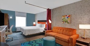 Ein Hotelzimmer mit Bett, einer Couch, einem Schreibtisch, einem Stuhl, einer Lampe und einem Fenster.