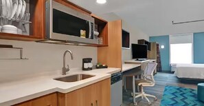 A modern kitchen with a microwave, sink, and coffee maker. There is a television and a bed in the adjacent room. - Home2 Suites By Hilton Savannah I95 North (Port Wentworth)