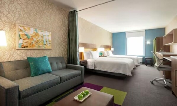 Ein Hotelzimmer mit einer Schlafcouch, einem Bett, einem Schreibtisch und einem Gemälde an der Wand.