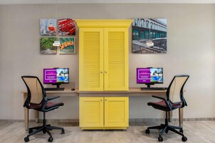 Um espaço de trabalho com duas mesas, cada uma com um computador e uma cadeira ergonômica. Um armário amarelo com duas portas está localizado no centro.
