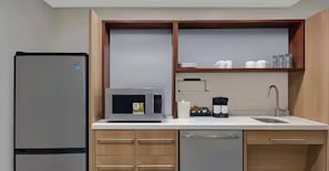 Une cuisine compacte équipée d’un réfrigérateur, d’un four à micro-ondes, d’un évier et de meubles de rangement en bois.