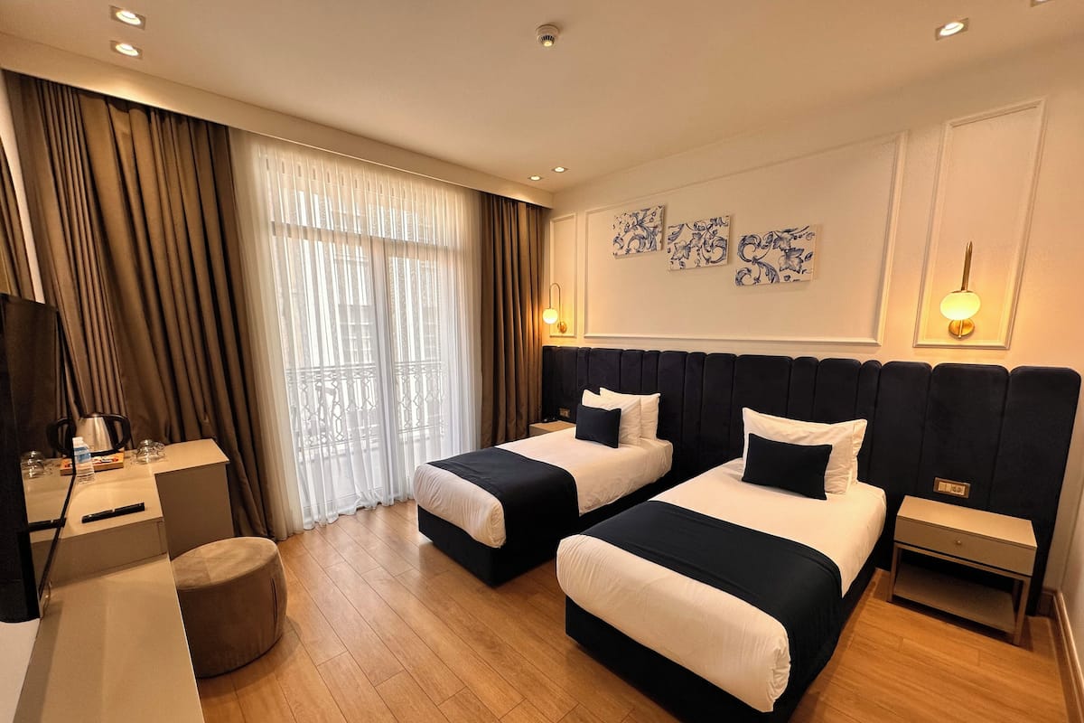 A hotel room with two beds, a desk, a chair, a TV, and a window with curtains.