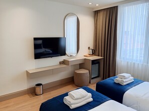 A hotel room with a flat-screen TV, a mirror, a coffee maker, a small refrigerator, a waste bin, and two beds with towels. - Taksim Bosphorus Hotel (Istanbul)