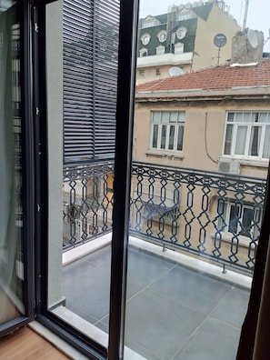 A balcony with a metal railing, a view of a building with a tiled roof, and a door with a glass panel. - Taksim Bosphorus Hotel (Istanbul)