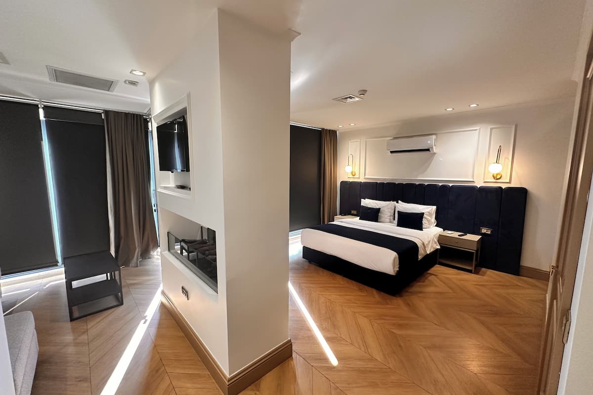 A modern hotel room with a large bed, built-in TV, air conditioning, and a view of the city.