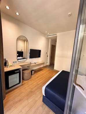 Une chambre d’hôtel moderne équipée d’un lit, d’un petit bureau, d’une télévision et d’un miroir.