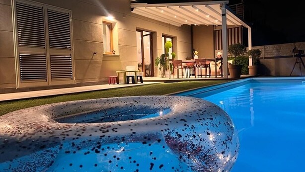 Ein Swimmingpool mit einem großen Luftreifen, einer überdachten Terrasse und einem Gebäude im modernen Stil.