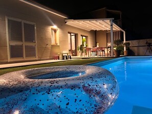 A swimming pool with a large inflatable ring, a covered patio area, and a building with a modern design.