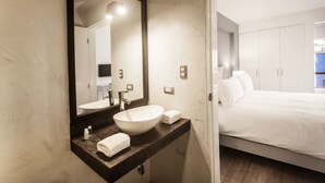 A modern bathroom with a large mirror, a white sink, and a bed with white linens.
