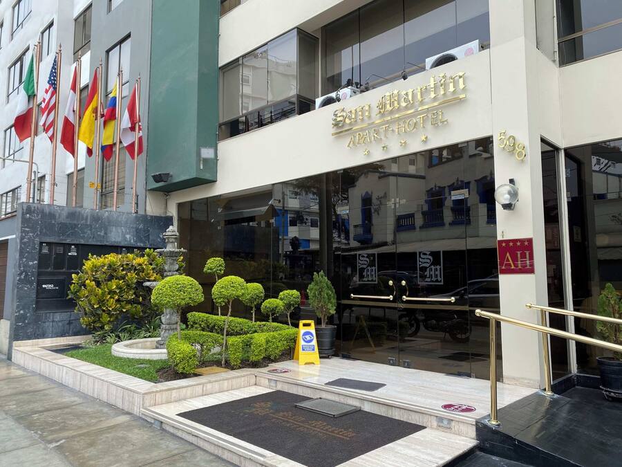 Entrada de un hotel con un letrero que dice 'San Martin Apart-Hotel' y banderas de varios países.