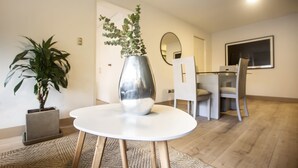 A modern living room with a round white table, a potted plant, and a large mirror on the wall.