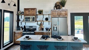 Cocina moderna con armarios de madera, una isla central con taburetes de bar, electrodomésticos de acero inoxidable e iluminación colgante.