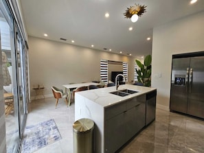 A modern kitchen with a central island, stainless steel appliances, and a dining area with a table and chairs. - Villa at The Grove (Miami)