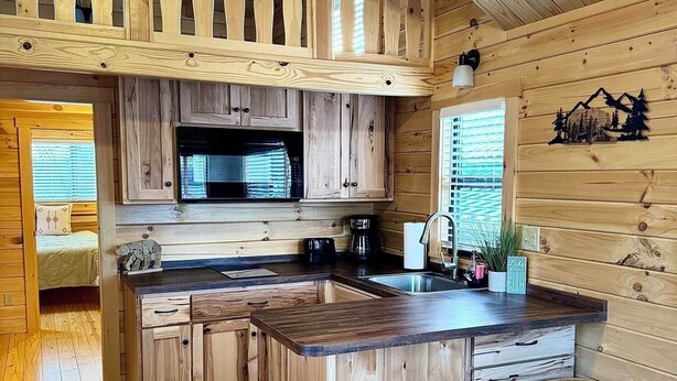 A wooden cabin interior with a kitchen featuring a central island, stools, and a dining area. - Cozy Cabin with Private Resort Amenities: Walking Distance to Lake James (Marion)