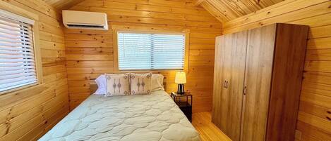 A wooden cabin room with a bed, a wardrobe, and an air conditioning unit.
