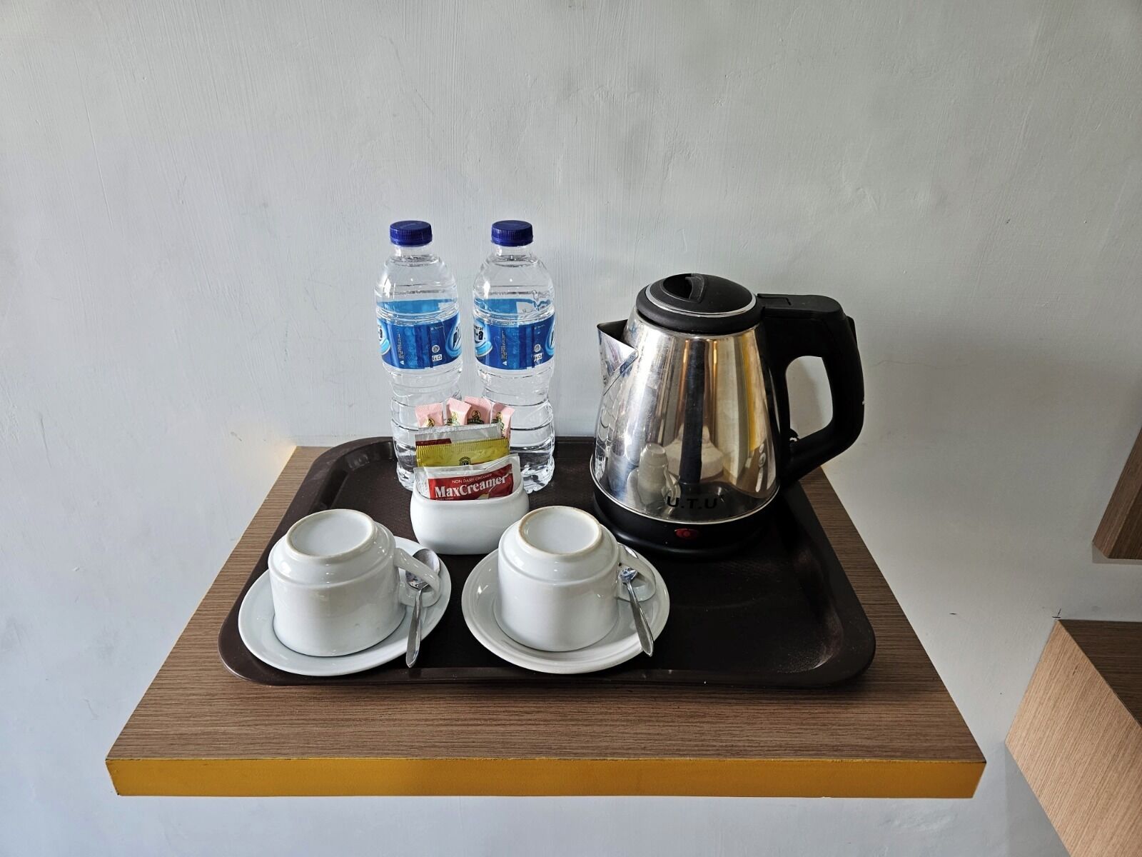 A tray with two white cups, two water bottles, a MaxCreamer container, and a black electric kettle.
