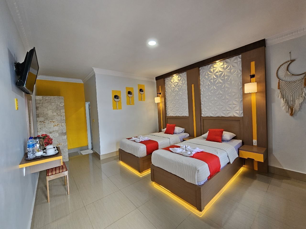A hotel room with two beds, a TV, a small table with a tray of breakfast items, and decorative wall panels.