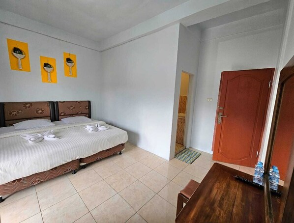 Une chambre d’hôtel avec un lit double, un banc en bois, une porte et une petite table sur laquelle se trouvent des bouteilles d’eau.