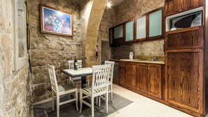 Une cuisine aux murs de pierre, avec des meubles de rangement en bois, une table à manger entourée de chaises et un tableau accroché au mur.