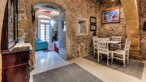 Une pièce aux murs de pierre, avec une table et des chaises, un buffet en bois et, au fond, un canapé bleu.