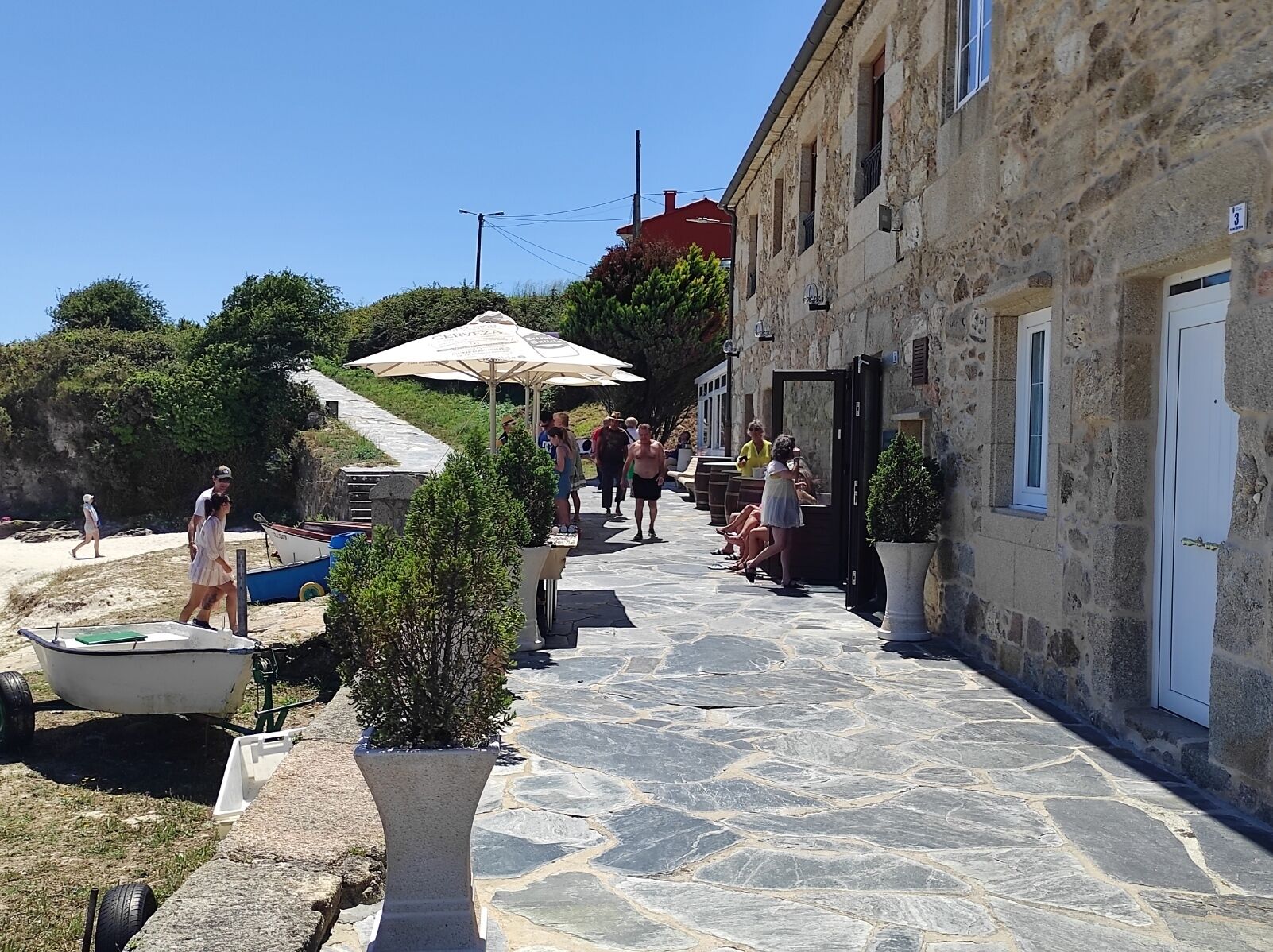 A stone-paved street with a row of buildings, outdoor seating, and a small boat.