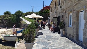 A stone-paved street with a row of buildings, outdoor seating, and a small boat. - The apartment is located in front of Langosteira beach, with stunning views. (Fisterra)
