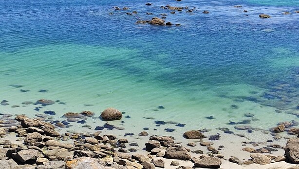 A rocky shoreline with clear blue water and distant hills. - The apartment is located in front of Langosteira beach, with stunning views. (Fisterra)