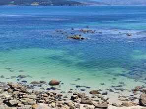 Una costa rocosa con aguas azul cristalinas y colinas a la distancia.