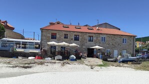 A stone building with a red-tiled roof, outdoor seating with umbrellas, and a sandy beach area. - The apartment is located in front of Langosteira beach, with stunning views. (Fisterra)