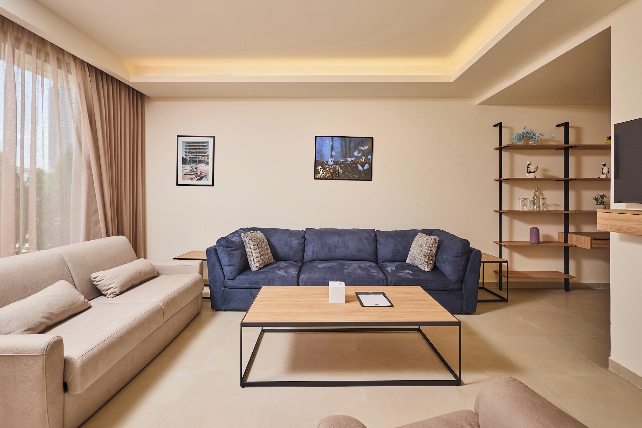 A modern living room with a beige sofa, a blue sofa, a wooden coffee table, and a bookshelf.