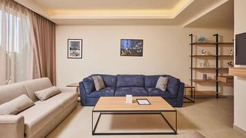 A modern living room with a beige sofa, a blue sofa, a wooden coffee table, and a bookshelf.