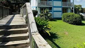A two-story hotel with a wooden deck leading to the entrance, surrounded by greenery and a clear blue sky. - Studio Relax Manganao, Proche de la plage et accès a la piscine (Saint-François)