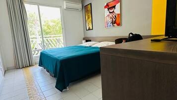 A hotel room with a bed, a desk, a chair, a TV, and a balcony with curtains.
