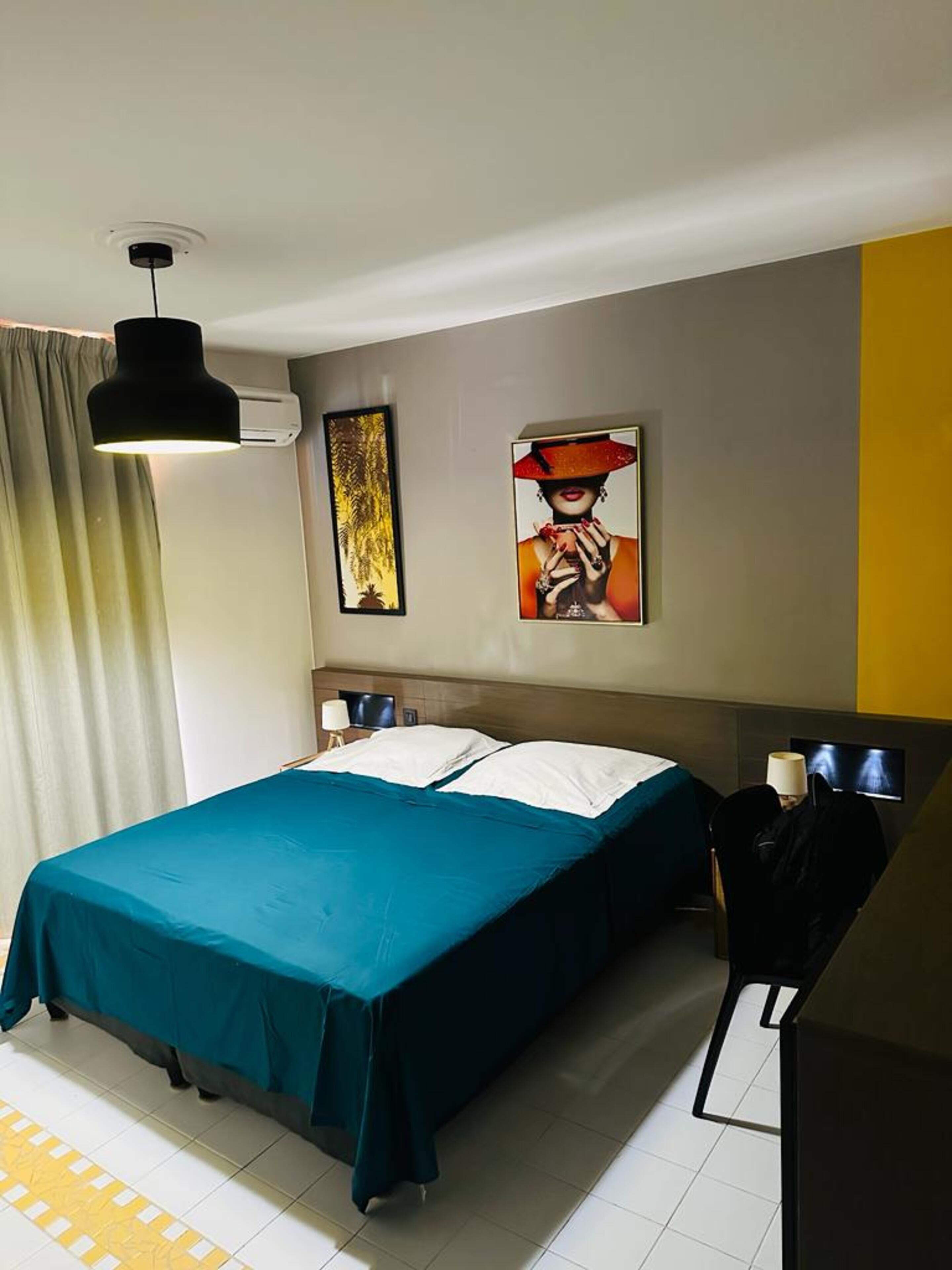 A hotel room with a bed, a desk, and a chair. There are two paintings on the wall.