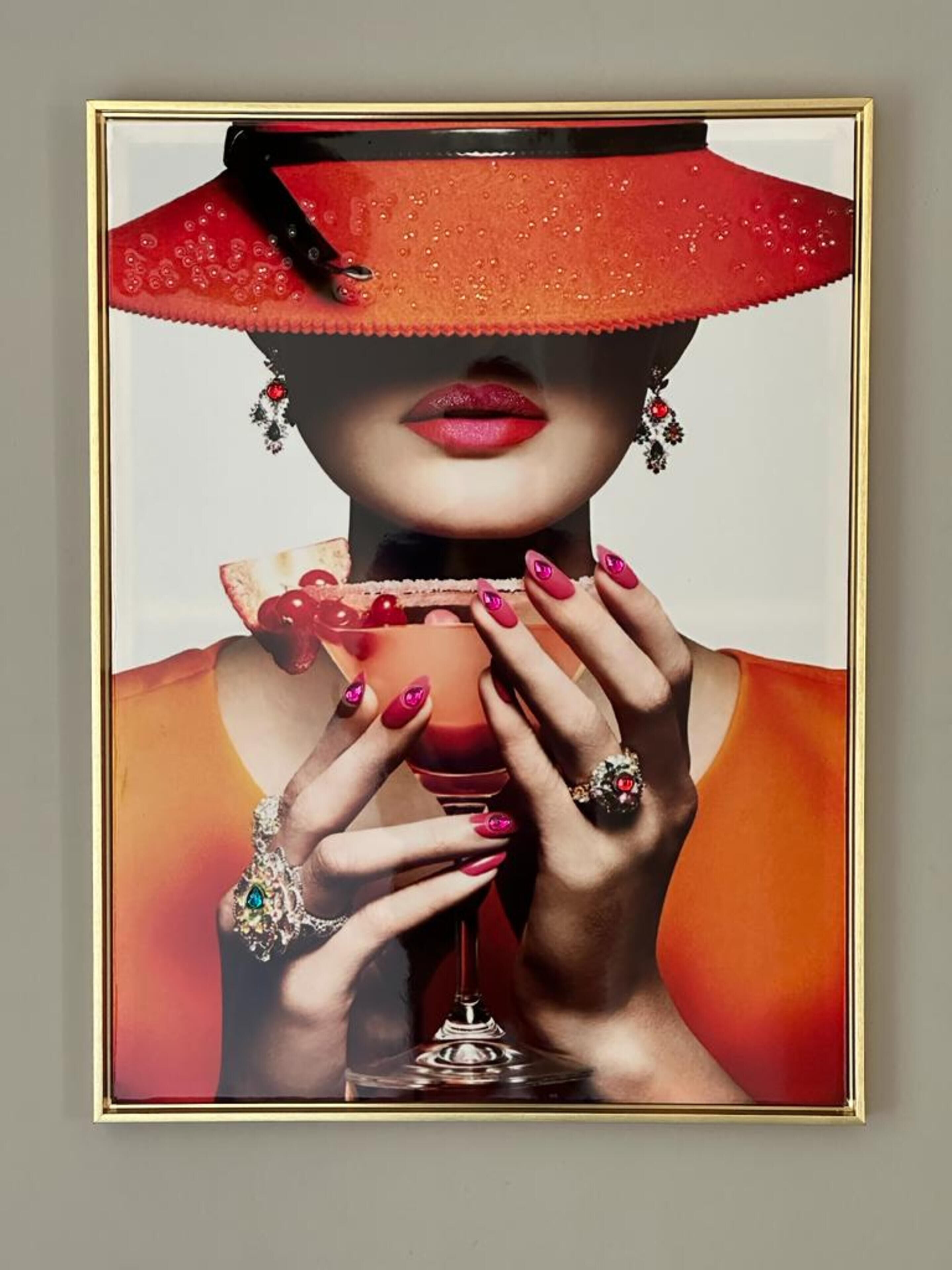 A framed artwork of a person holding a drink with a red hat and earrings.