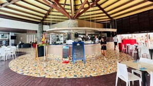 An indoor area with a high ceiling supported by wooden beams, a patterned floor, and a central counter with a menu board. - Studio Relax Manganao, Proche de la plage et accès a la piscine (Saint-François)