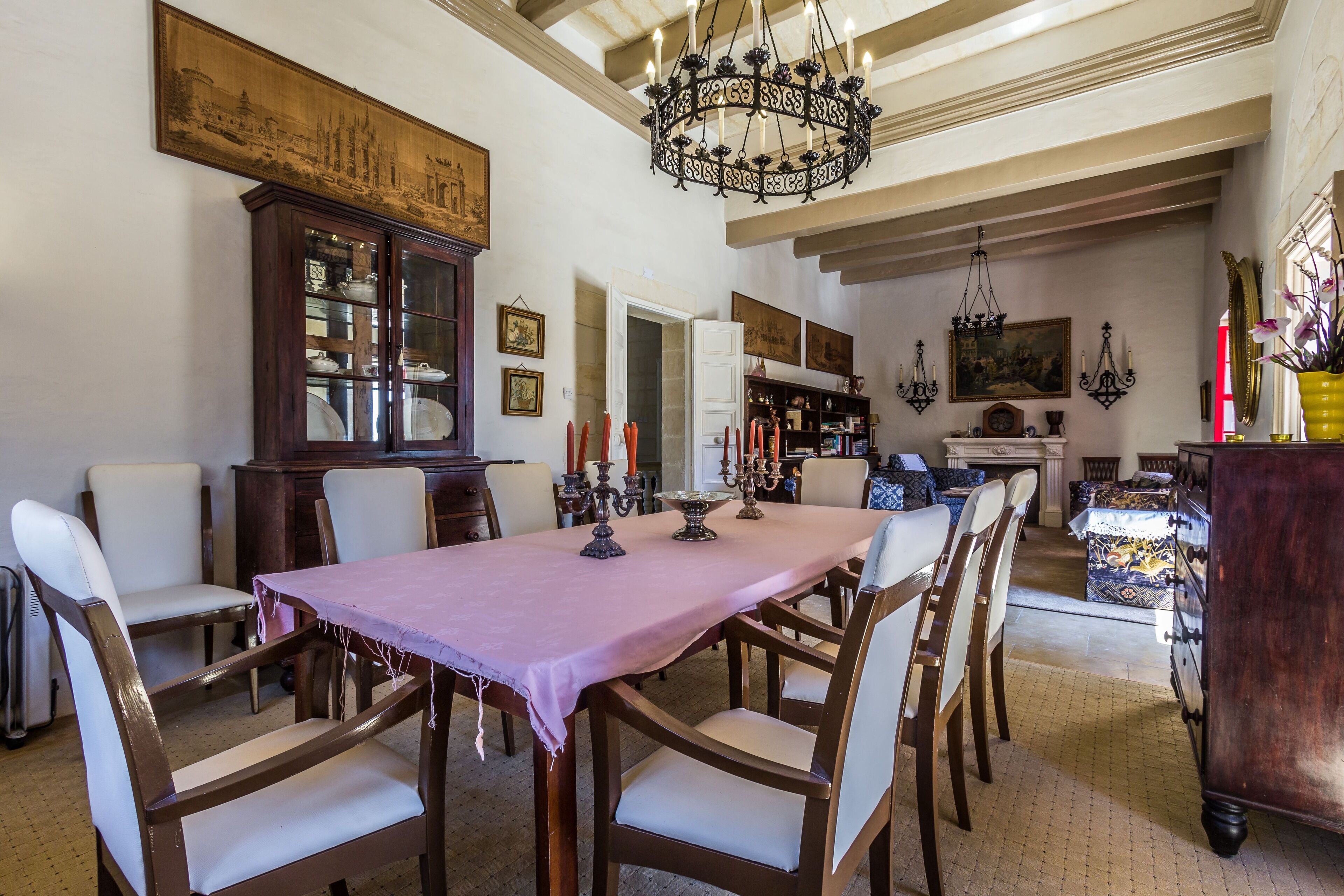 A dining area with a long table, chairs, a chandelier, and a cabinet with glass doors.