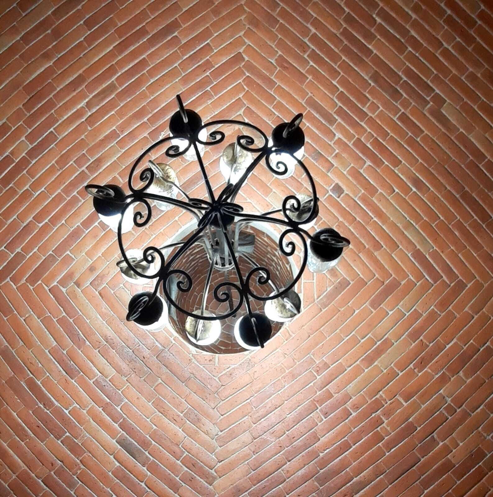 A circular ceiling light fixture with a central bulb and four smaller bulbs, mounted on a brick wall.