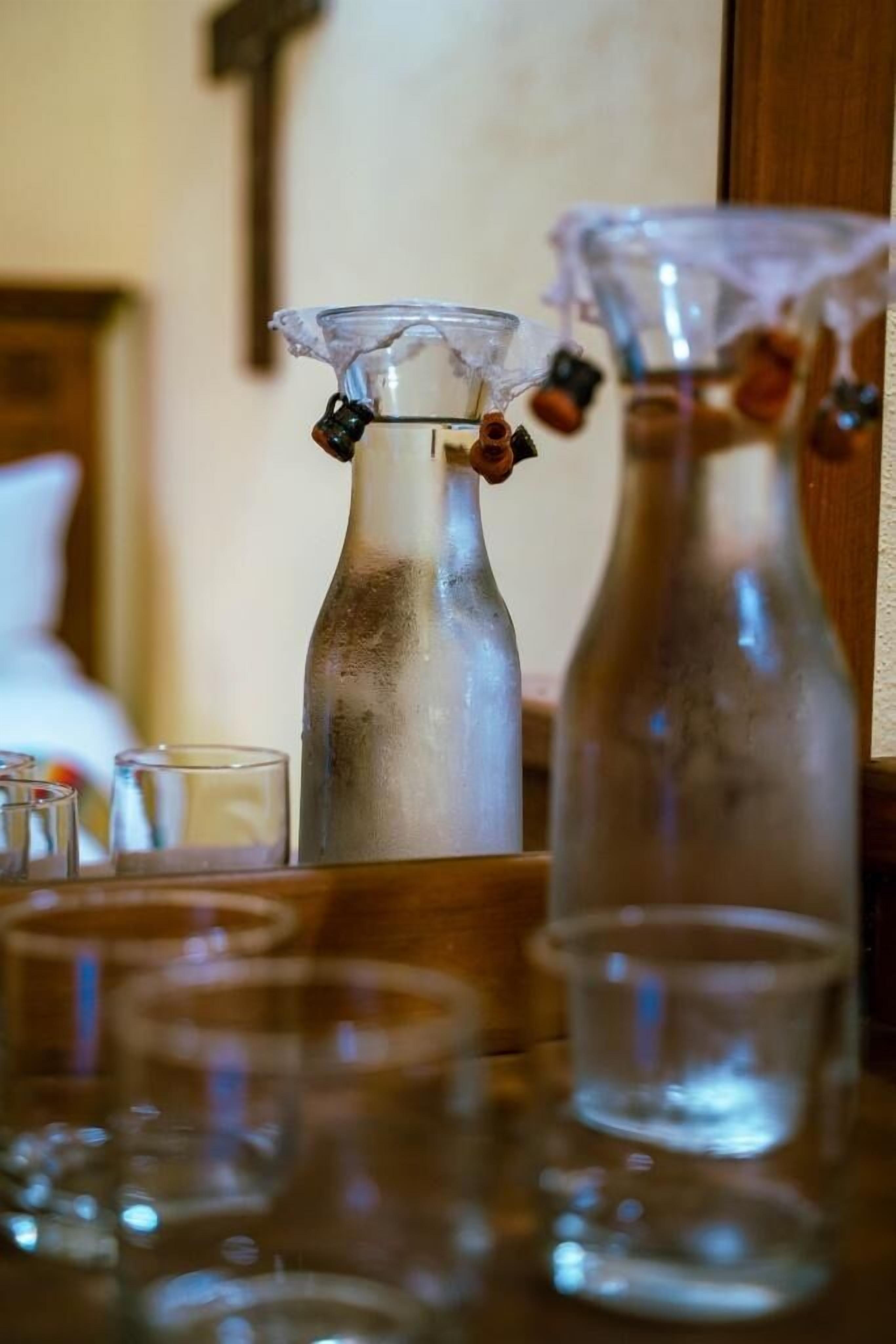 A room with a wooden table holding several clear glasses and two glass bottles with metal caps.