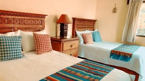 A hotel room with two beds, each with patterned bedding and a wooden headboard. There is a nightstand with a lamp between the beds. - CASONA DOS VIDAS (Tequisquiapan)