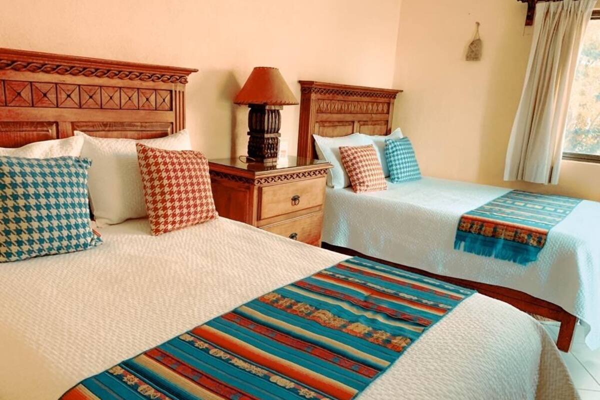 A hotel room with two beds, each with patterned bedding and a wooden headboard. There is a nightstand with a lamp between the beds.
